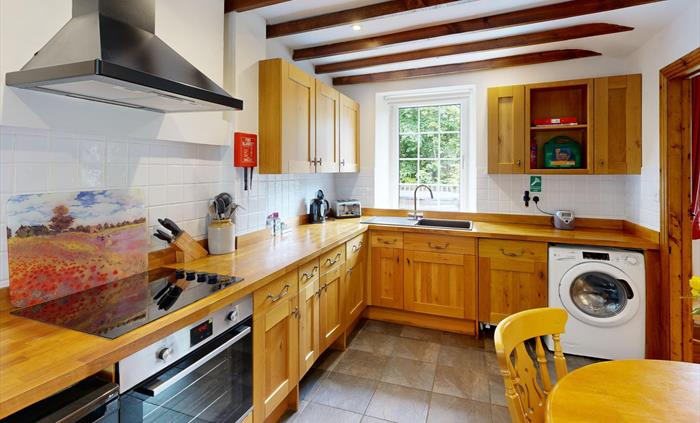 Warm wooden kitchen with beamed ceiling, electric hob, and countryside views through the window.